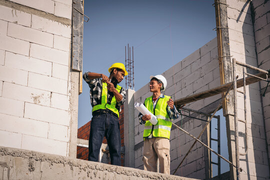 Construction Workers Discussing Building Plans on Site with Safety Gear Asian Men Analyzing Blueprint for New Build Project Civil Engineering Design