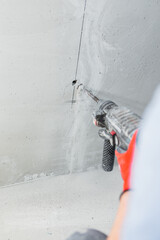 Closeup of worker hand with hammer drill while drilling wall - electrical wiring installation and chasing
