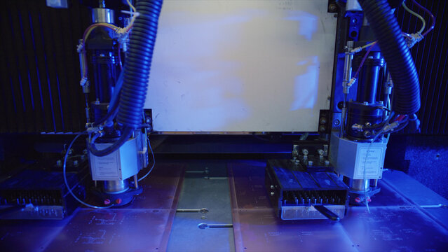 Automated industrial laser engraving machine cutting through electronic circuit boards, casting a vibrant blue light in a modern manufacturing facility, showcasing advanced technology and precision - Powered by Adobe