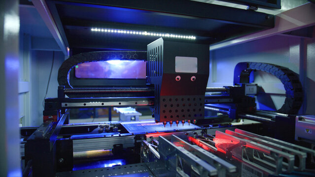 Surface mount technology - smt - machine placing electronic components on a printed circuit board - pcb - illuminated by red and blue lights in modern factory