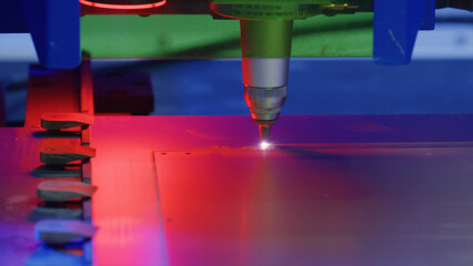 Industrial laser engraving machine cutting a metal plate, emitting a red light during the process,...