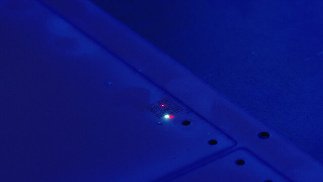 Close up of an electronic device emitting a red and green light, featuring a qr code, bathed in a mysterious blue light, suggesting technological advancement or data transmission