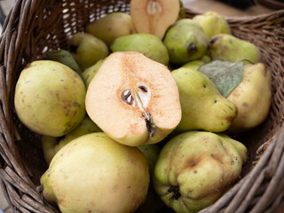 Pile of ripe quinces in a rustic wicker basket with a cut half in the foreground