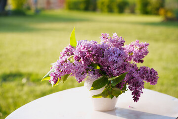 A bouquet of lilacs in a white vase on a garden table