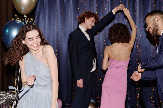 Group of teenagers dancing at party, smiling Caucasian girl in foreground enjoying music, multiethnic teenagers in formal attire celebrating together with balloons and festive backdrop