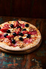 Pizza with ham, salami, tomatoes and mozzarella cheese. Rustic wooden background. Soft focus. Close up.	