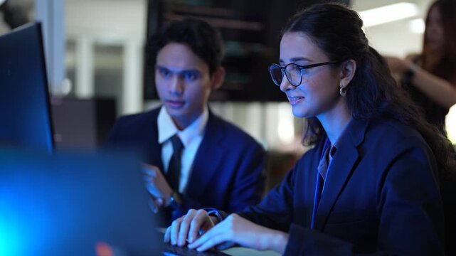 A happy team of young professionals discusses a new idea in a modern office. The smiling man presents his plan on a tablet to his colleagues during a creative meeting at night.
