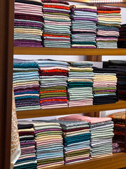 Stacks of colorful fabrics arranged neatly on wooden shelves. Textile trade, cultural heritage, and traditional craftsmanship in everyday marketplace.