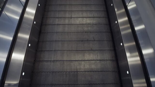 Closeup of metallic escalator steps with illuminated side lights forming repeating pattern in urban interior