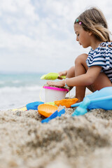 Child playing with colorful toys on the sandy beach during a cloudy day by the ocean