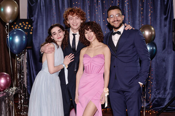 Group of teenagers posing together at formal event, smiling at camera, balloons and confetti in background  © AnnaStills