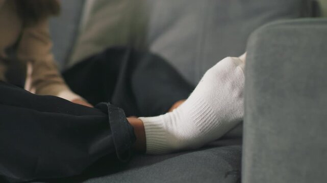 Close-up of girl s feet in white socks resting on couch. Cozy indoor moment, relaxed posture, focusing on comfort and calm at home, creating peaceful, domestic atmosphere