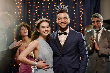 Caucasian teenage girl and teenage boy wearing crowns standing together smiling at camera during...