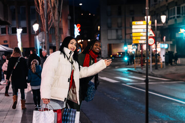 Women waving for taxi after holiday shopping in festive city. Christmas. Celebration.