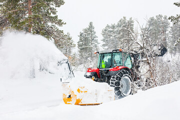 Essential work unfolds in extreme cold as a snowblower equipped tractor carves through deep snow,...