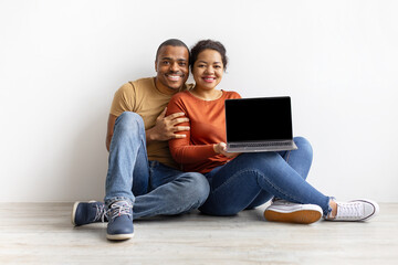 African American couple sitting on floor together with laptop in lap, smiling. Concept of digital technology, communication, online connection, and modern lifestyle, mockup
