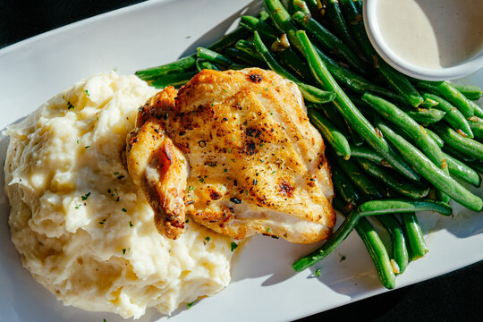 Smoked chicken with green beans and mashed potatoes on a white plate with a side of ranch against a black background