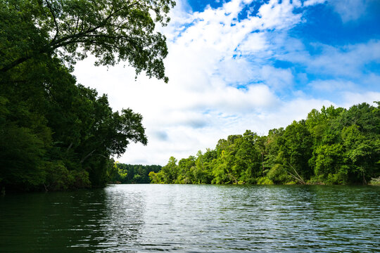 A stretch of the Catawba River near Charlotte, North Carolina in summer, lined on both sides with green forests with clouds and blue skies above.