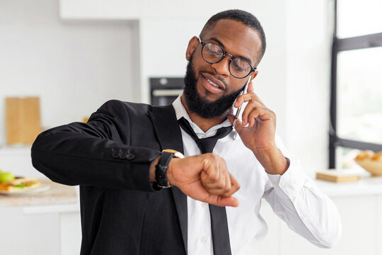 Morning Rush. Busy African American business man worker in eyeglasses talking on smart phone at home, wearing suit and looking at wrist watch, getting ready, going to office in a hurry, being late