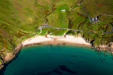 Aerial top down shot of Keem Beach showing calm blue ocean waves and parked vehicles on a bright sunny day