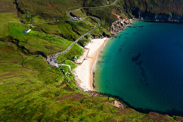 Aerial view of Keem Beach with calm blue Atlantic waters, cars parked along the road, and a winding mountain road in County Mayo	