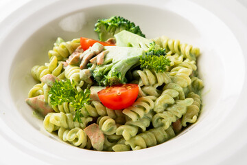 Close-up of rotini pasta with green pesto sauce, broccoli, cherry tomatoes, and parsley on a white...
