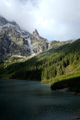 Calm mountain lake reflects dense forest and sharp rocky peaks, serene wilderness landscape...