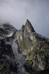 Sharp rocky peak rises into misty sky, dramatic mountain landscape shows strength of nature, steep cliffs and rugged textures highlight wild untamed beauty of highlands.
