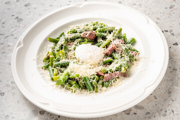 Plated dish with green vegetables, sliced beef, poached egg, and grated cheese. Gourmet presentation on white plate. Top view, homemade meal, rustic countertop.