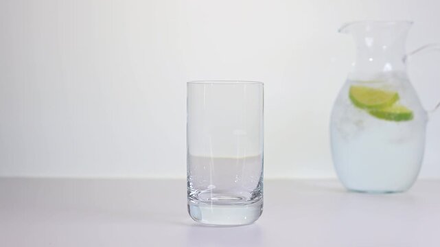 Trinkglas mit Mineralwasser und Limonenscheibe und Eisw&uuml;rfeln