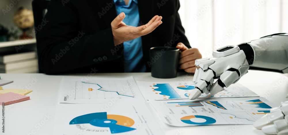 Poster a human and a robot interact at an office desk, examining charts and data reports together while enj