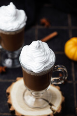 Hot drink with whipped cream and pumpkin on dark background