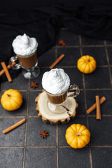 Autumn coffee drink with whipped cream, mini pumpkins, cinnamon sticks, and star anise on a dark...