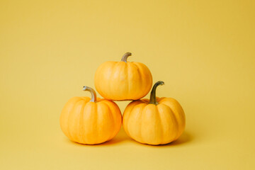Three small bright orange pumpkins stacked neatly on a plain bright yellow background
