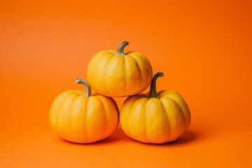 Three orange pumpkins stacked in a pyramid on a bright orange background