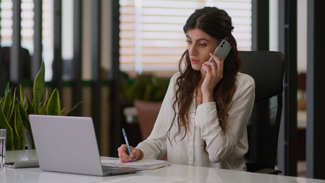 Caucasian business woman busy female businesswoman office girl planner organizer talking mobile phone conversation cellphone chatting client order e-commerce write notebook manage tasks work laptop - Powered by Adobe