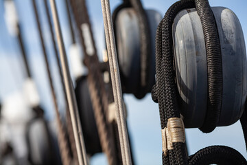 Tradition of sailing navigation. Nautical rigging with grey blocks and ropes on a sailing vessel against blue sky. Maritime ship equipment closeup.
