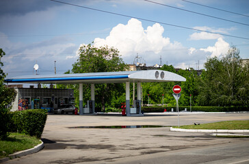 An everyday scene of a gas station with a "no entry" sign and a parked car under a dramatic cloudy sky. The puddles on the pavement suggest recent rain, creating a quiet, moody urban landscape.

