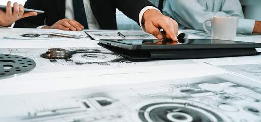 A dynamic scene showcasing business professionals engaged in a collaborative design project. The image highlights a digital tablet and blueprints on a modern office table. SACTR