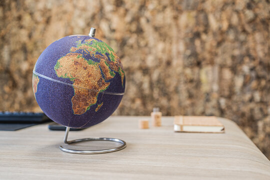 Cork globe standing on a desk with cork wall background in a modern office interior.