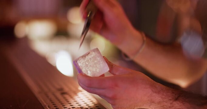 Pub ice. Preparing cold drink. Bartender hand using chipper making textured huge cube for refreshing cocktail. Professional bar picks chisel.