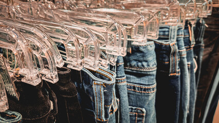 close-up view of several pairs of blue denim jeans hanging on clear plastic hangers at an angle....
