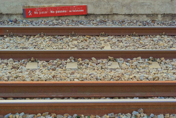 Close-up view of railway tracks with a red multilingual warning sign that says “No...