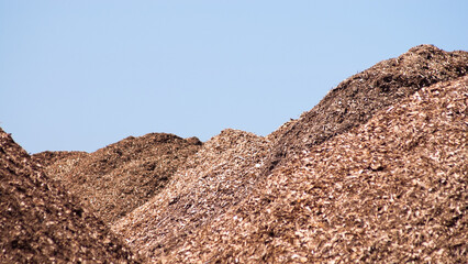 mountains of wood chips against the blue sky and green forest