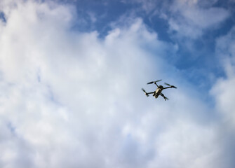 A drone takes pictures from the sky, drone reconnaissance, on a blue sky background. Flying drone on the sky with clouds. An unmanned aerial vehicle ( UAV ) or quadcopter drone fly with four rotors. 