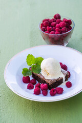 Chocolate brownie dessert with ice cream, min,t and raspberries on a white plate. 