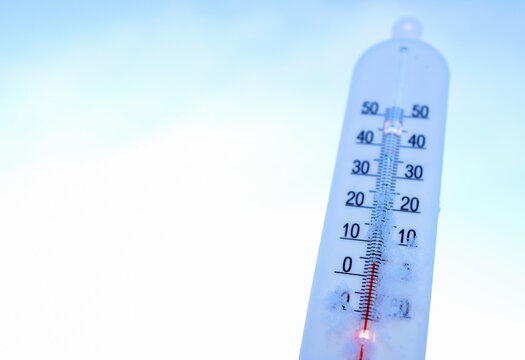 Thermometer on winter snow on blue sky. Thermometer for measuring outdoor air temperature. Cold weather in winter season. Meteorological device for observing, measuring the weather. Weather forecast.