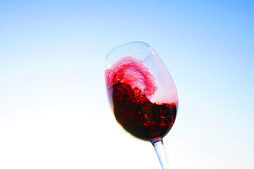 Red wine swirling on blue sky. Sommelier swirls with glass of red wine at sunset sky. Red Wine Swirling In Glass during vine Tasting, celebration vino party. Vibrant liquid splashing. Space for text