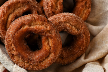 Closeup of a fresh baked batch of Apple Cider Donuts on a tea towel in a basket.