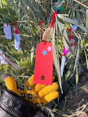 A yellow gloved hand holds a colorful paper wish hanging from the tree at the Japanese Garden in...